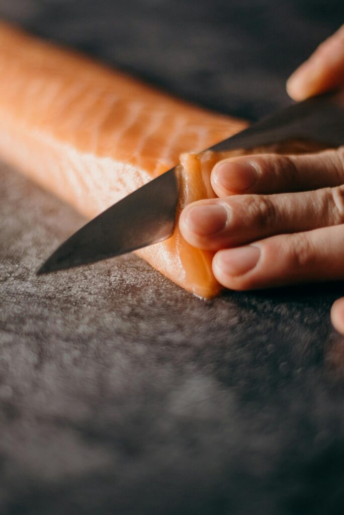 Close-up of hands skillfully slicing fresh salmon fillet on dark surface, showcasing culinary expertise.