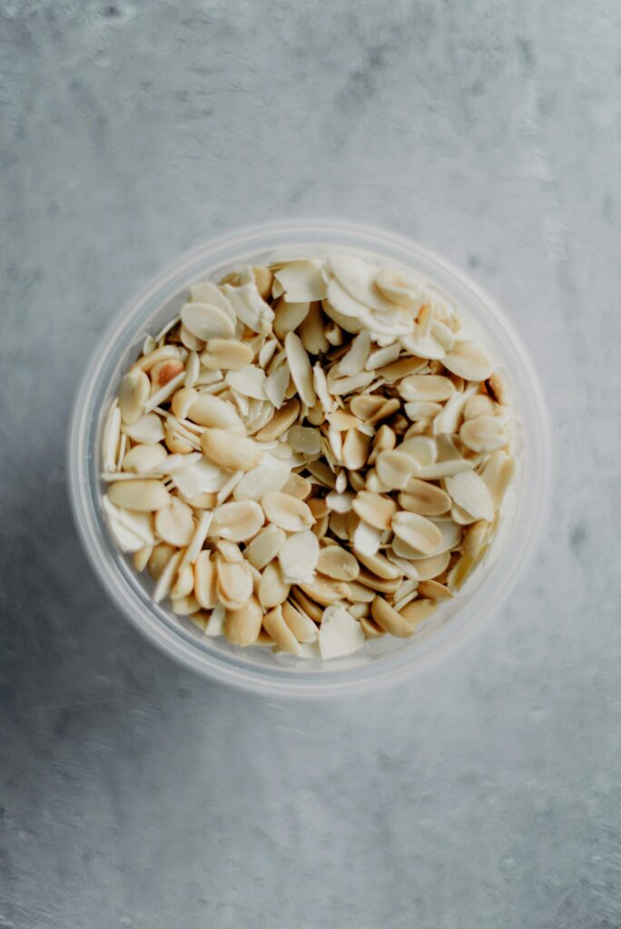 A clear bowl full of sliced almonds viewed from above on a textured surface.